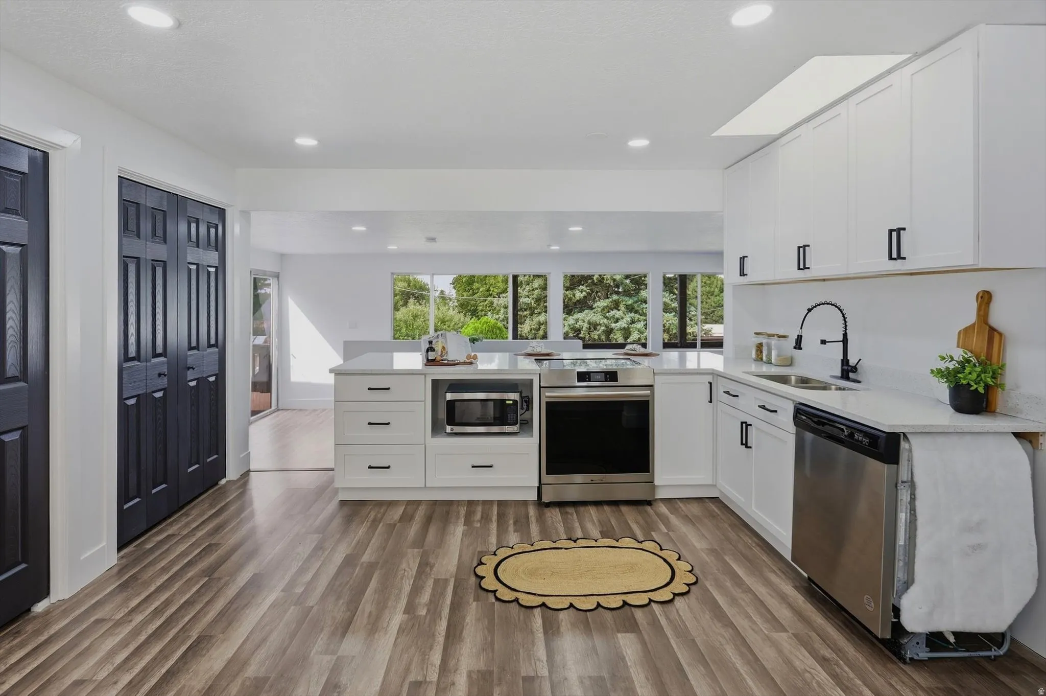 Modern kitchen featuring white cabinetry, light-colored countertops, stainless steel appliances, and wood-finish flooring