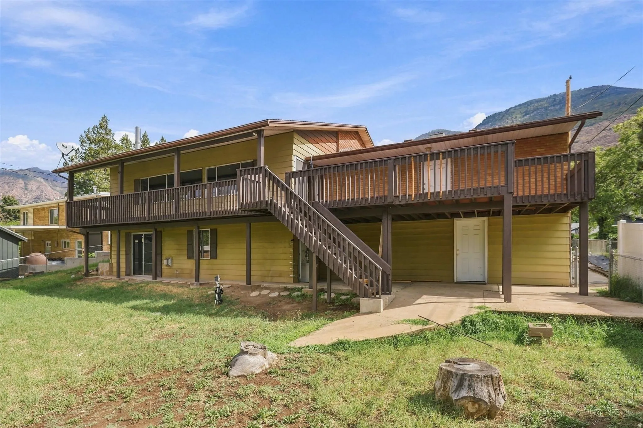 Two-story residence featuring an upper-level wood deck with railing, exterior staircase, ground-level patio, and a sliding glass door