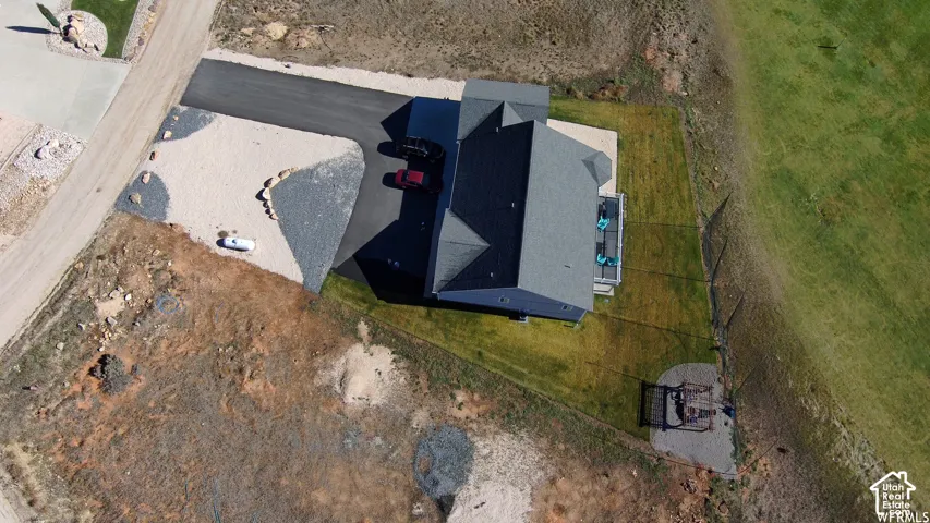Asphalt driveway, gravel landscaping, manicured lawn, built-in patio, and a shingled roof
