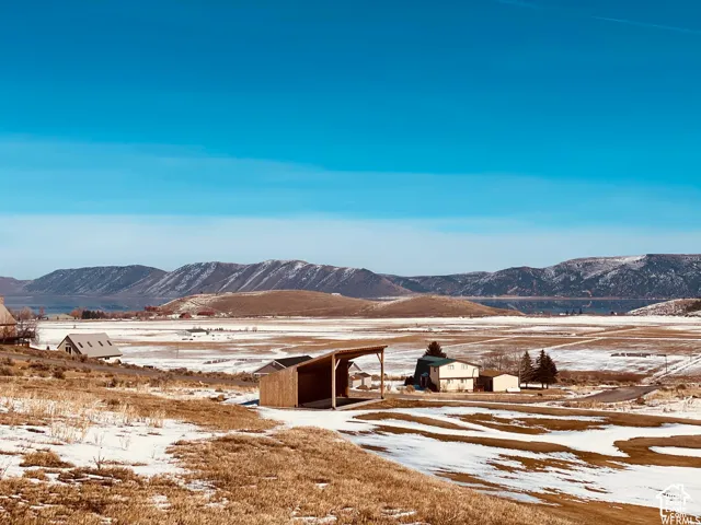 Expansive property featuring an open-sided shed structure, distant residential buildings, and a mountainous backdrop
