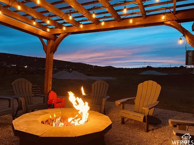 Wood pergola with string lights, a stone fire pit, and a gravel patio