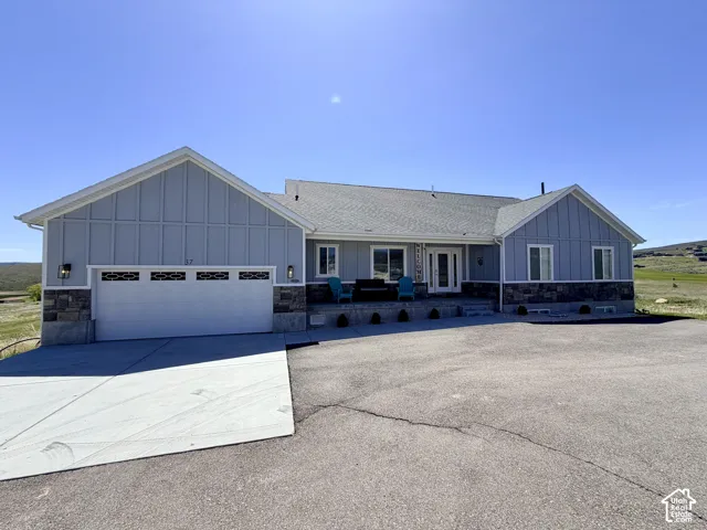 Light blue siding exterior with stone accents, a covered front porch, an attached garage, and a wide paved driveway