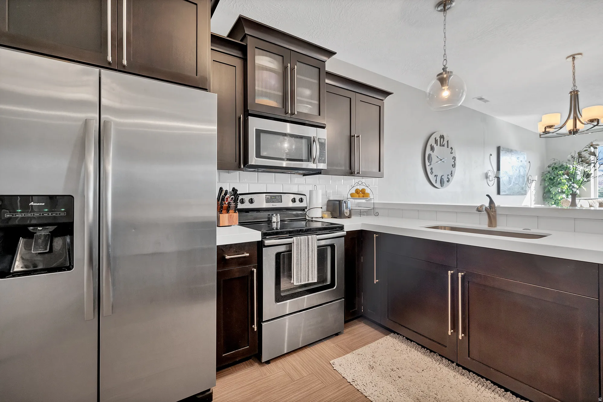 Stainless steel appliances, white subway tile backsplash, dark wood-finish cabinetry, light-toned countertops, and wood-finish flooring