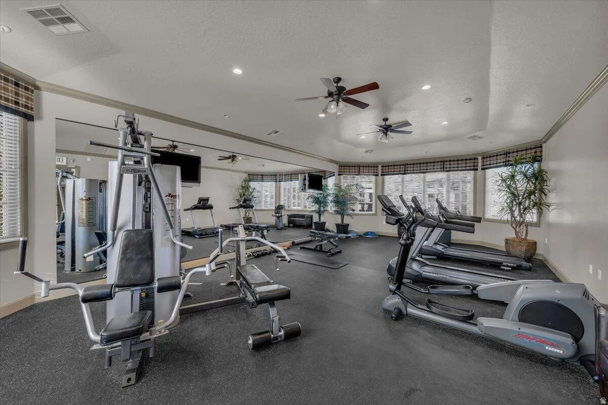 Dedicated fitness area featuring rubberized flooring, multiple exercise machines, ceiling fans, recessed lighting, and expansive windows with blinds