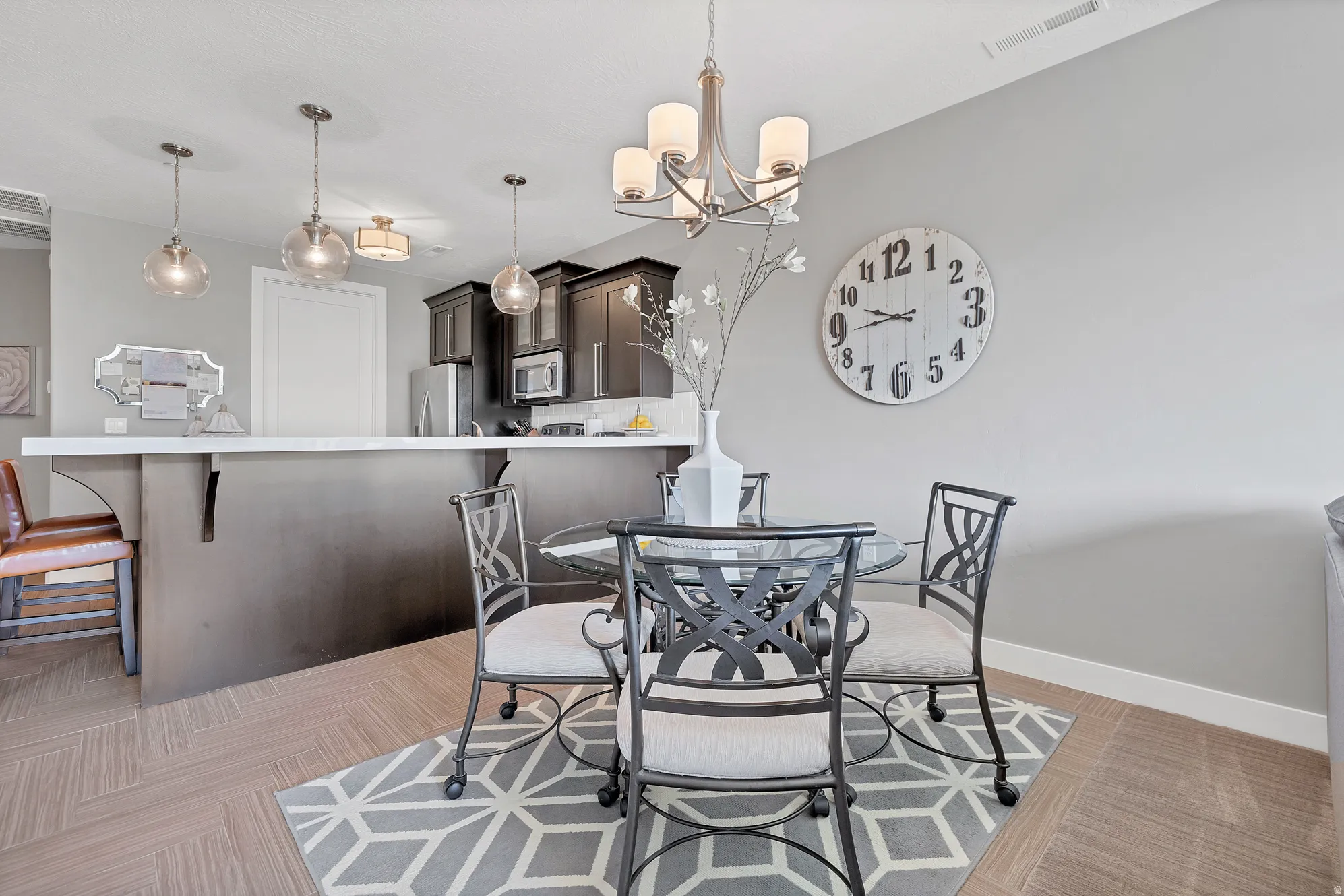 Open-concept dining area with wood-finish flooring, a contemporary chandelier, and a breakfast bar with pendant lighting