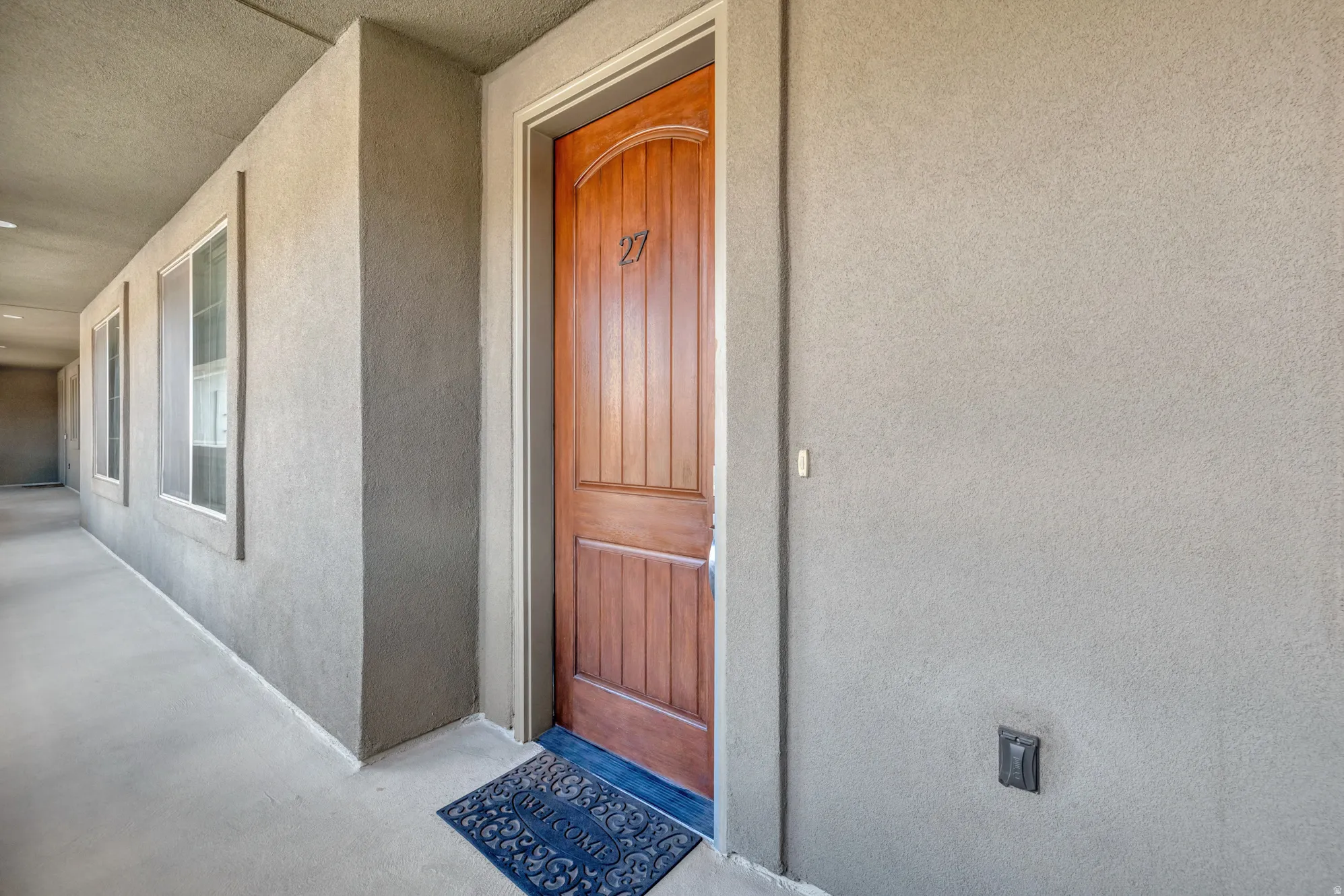 Arched wood-panel entry door with visible numbering, complemented by textured stucco walls and multiple corridor windows