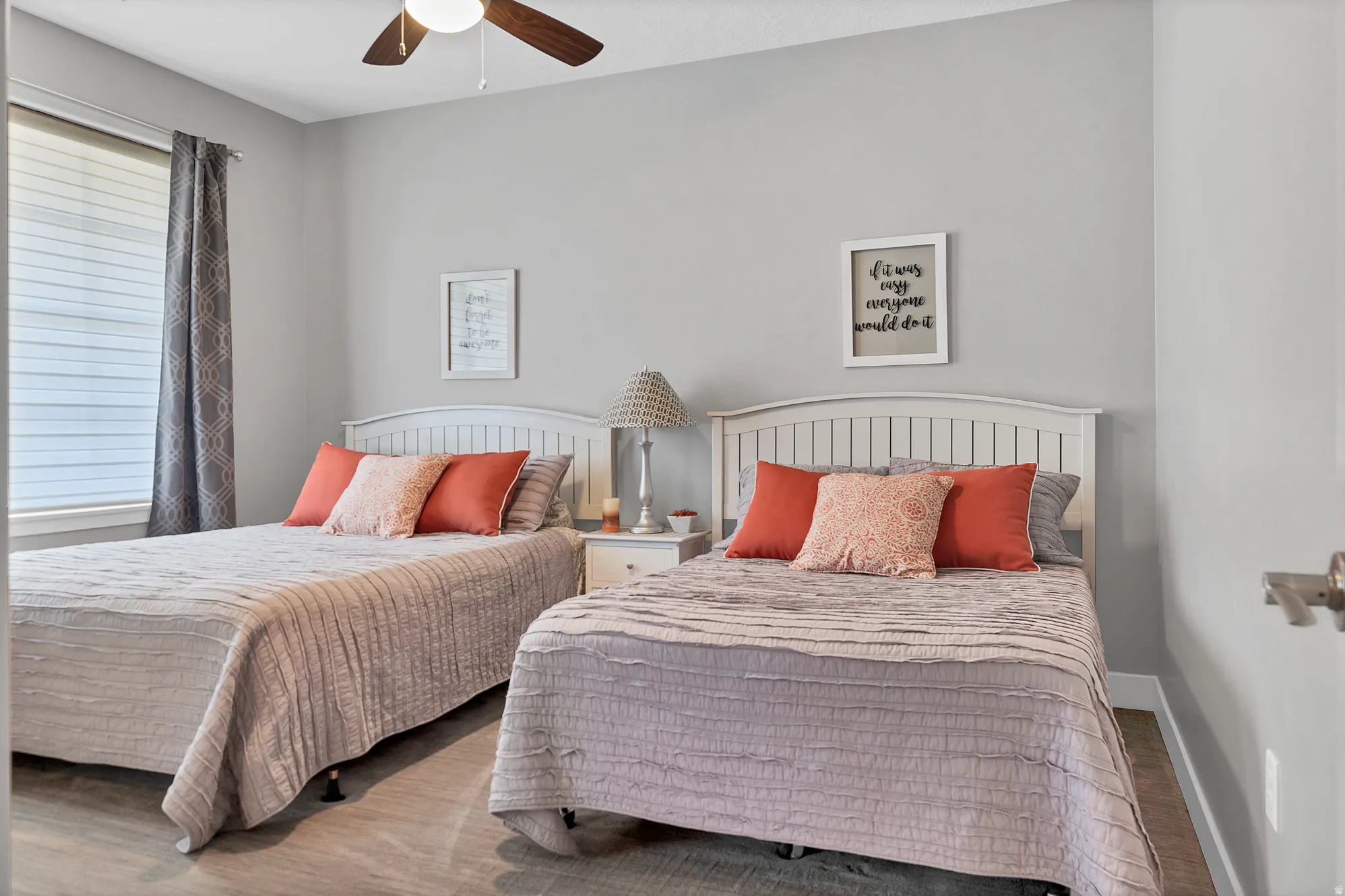 Wood-finish flooring, white headboards, a ceiling fan with integrated lighting, and a window with horizontal blinds