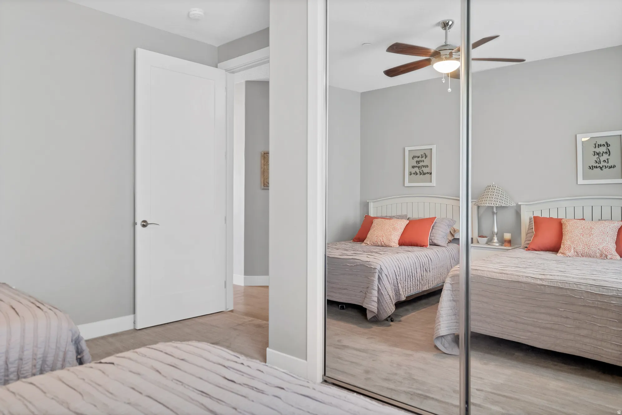 Light gray wall paint, wood-finish flooring, white paneled interior door, mirrored closet doors, and a ceiling fan with integrated lighting