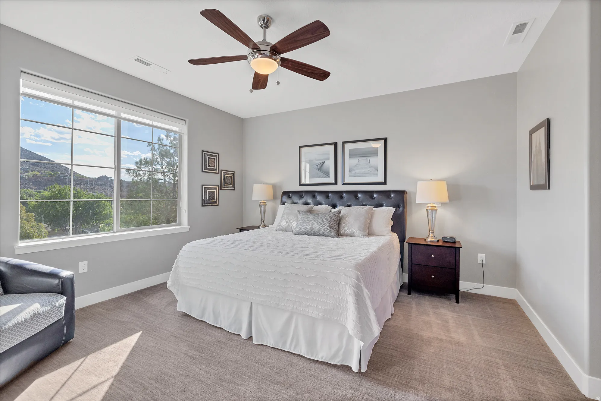 Expansive window with grid panes, textured wall-to-wall carpeting, ceiling fan with integrated lighting, and a built-in wall niche
