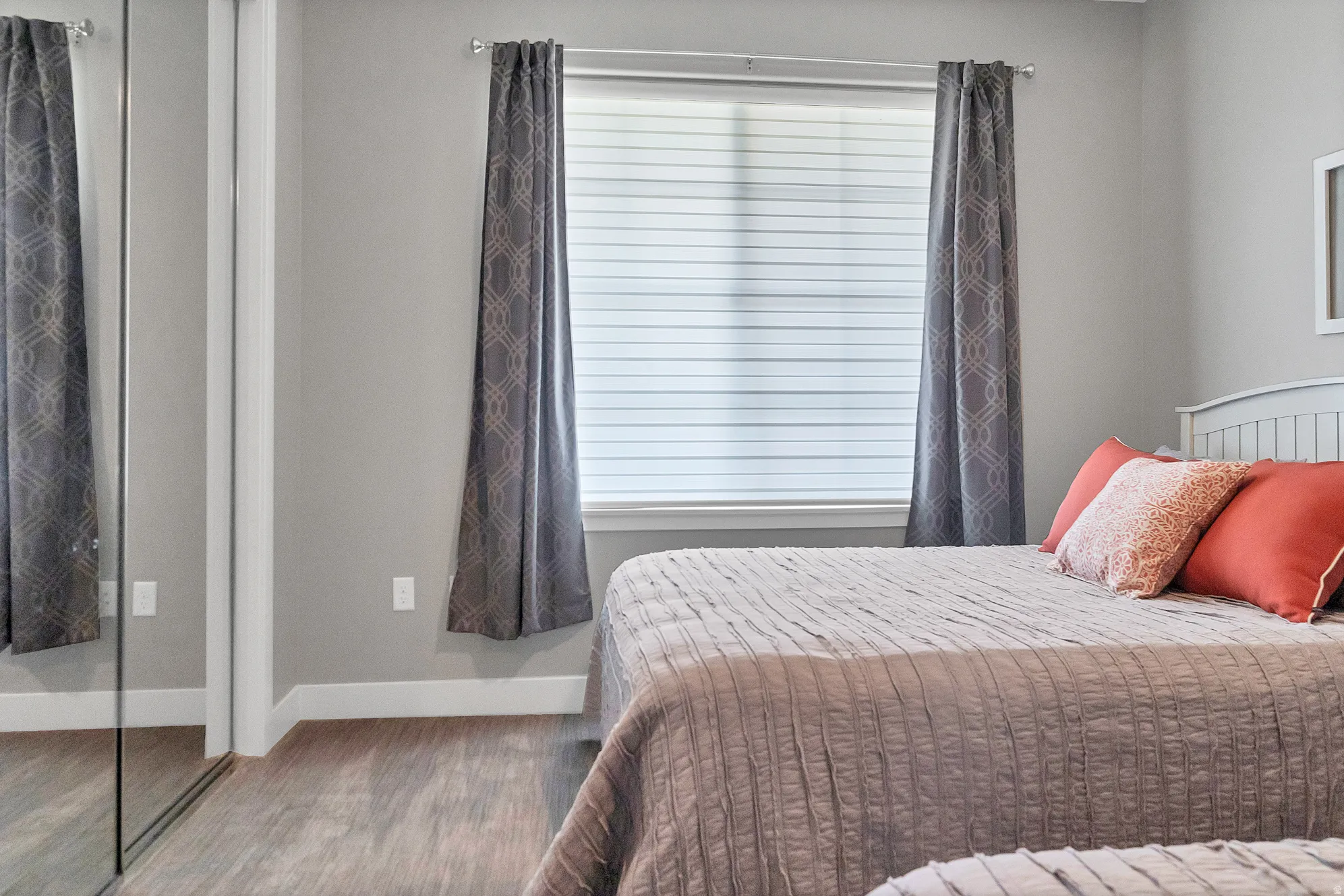 Mirrored closet doors, window with blinds and drapes, wood-finish flooring, and light gray wall paint