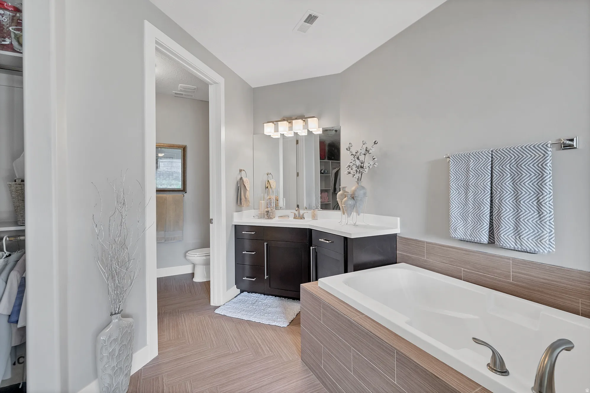 White drop-in bathtub with brushed nickel fixtures, wood-finish tile surround, and light gray wall paint