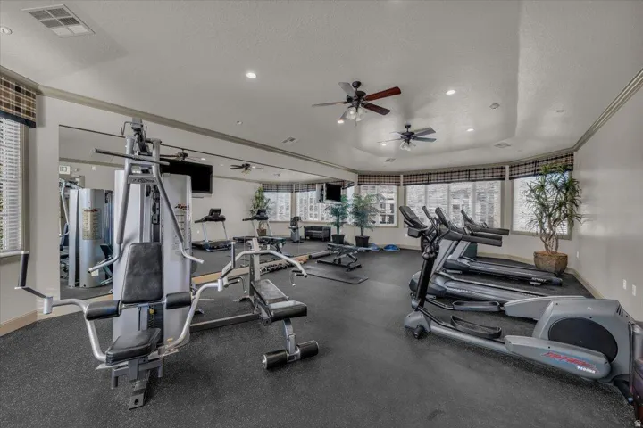 Dedicated fitness area featuring rubberized flooring, multiple exercise machines, ceiling fans, recessed lighting, and expansive windows with blinds