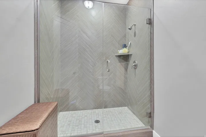 Frameless glass shower enclosure featuring a fixed showerhead, patterned wall tile, tiled flooring, and a built-in shelf