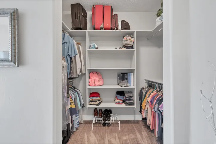 Walk-in closet featuring white built-in shelving, clothing rods, and wood-finish flooring