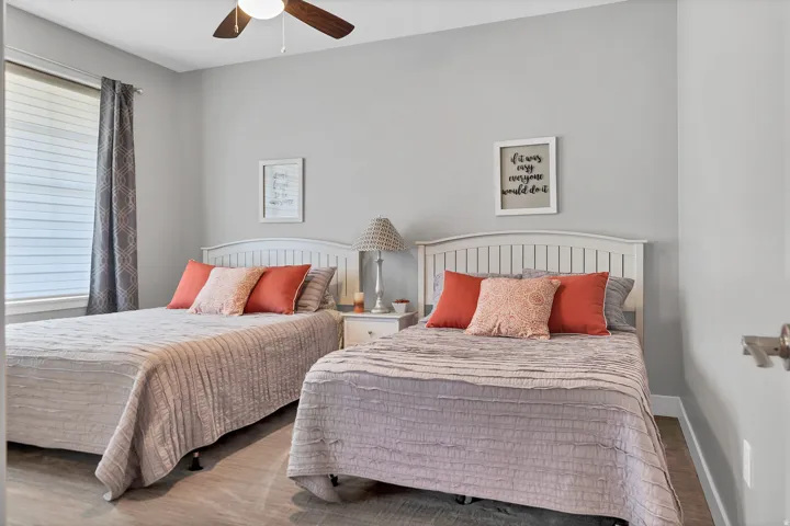 Wood-finish flooring, white headboards, a ceiling fan with integrated lighting, and a window with horizontal blinds