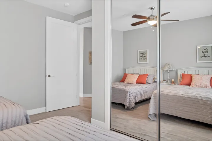 Light gray wall paint, wood-finish flooring, white paneled interior door, mirrored closet doors, and a ceiling fan with integrated lighting