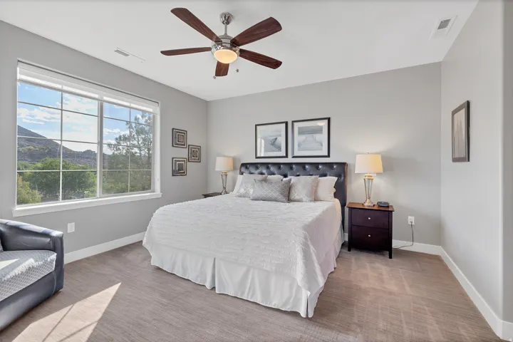 Expansive window with grid panes, textured wall-to-wall carpeting, ceiling fan with integrated lighting, and a built-in wall niche