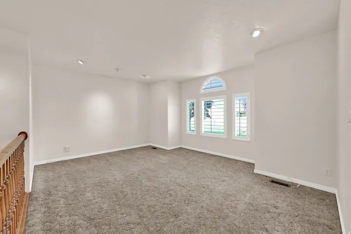 Recessed lighting illuminates the carpeted room, featuring three windows with plantation shutters and an arched transom window