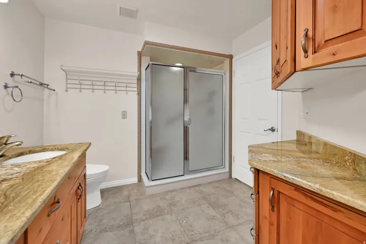 Dual wood-finish vanities with stone countertops, enclosed shower, and tile flooring
