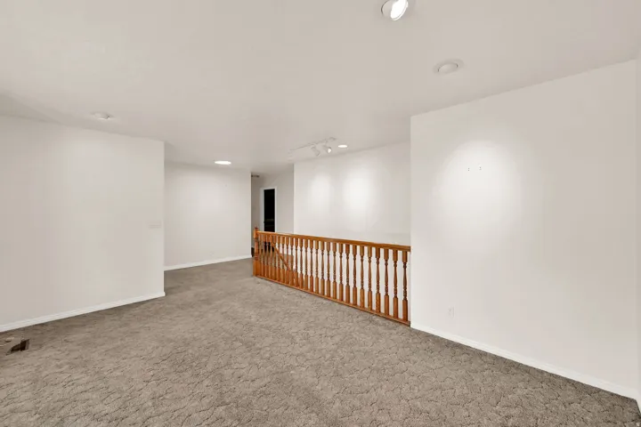Recessed ceiling lighting illuminates a carpeted landing featuring a wooden spindle railing