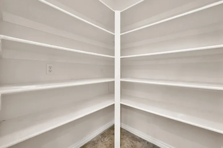Walk-in pantry with multiple tiers of built-in shelving, a central dividing support, and durable tile flooring