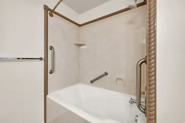 Tub-shower combination with a textured shower frame, light-toned wall panels, and integrated grab bars