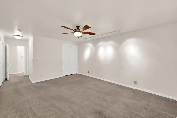 Spacious room featuring neutral carpeting, a ceiling fan, track lighting, and white bi-fold closet doors