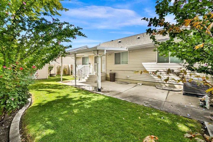 Expansive lawn area with mature landscaping, covered patio, and concrete hardscaping