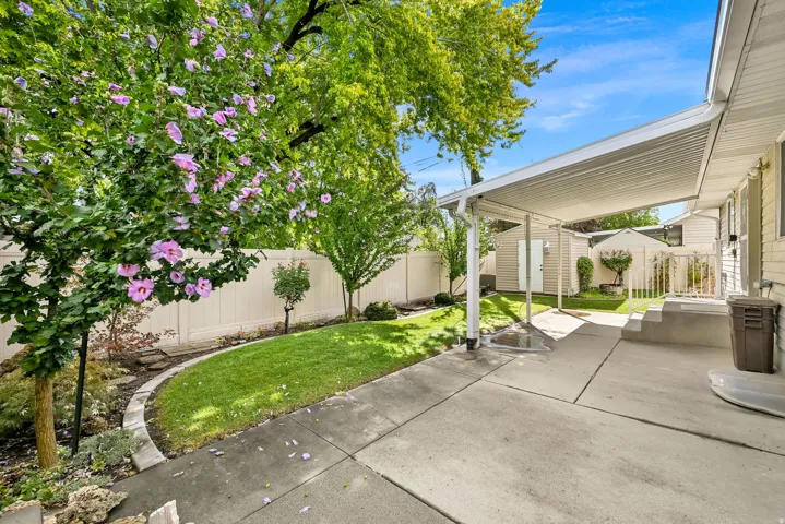 Covered patio with concrete surfacing, leading to a landscaped yard featuring a manicured lawn and mature plantings