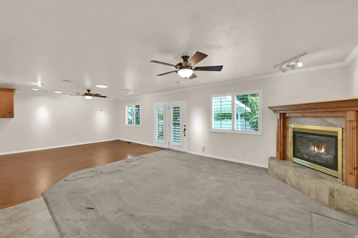 Wood-finish flooring and carpeted areas, a fireplace with a stone surround, and multiple ceiling fans