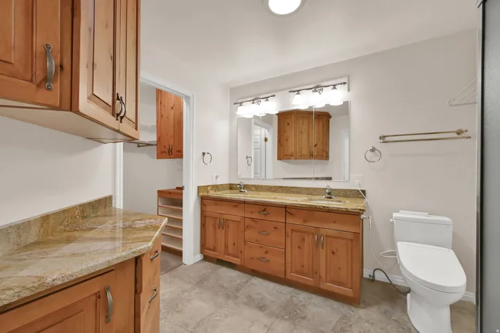 Dual vanity with granite countertops, wood cabinetry, and a mirrored medicine cabinet