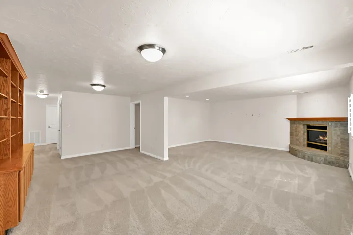 Spacious room featuring carpet flooring, built-in shelving, a stone-clad fireplace, and recessed lighting