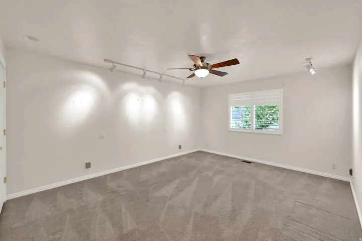 Recessed lighting, track lighting, ceiling fan with integrated light, window with white plantation shutters, and light-toned carpeting