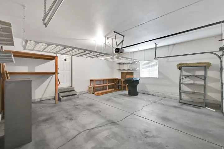 Concrete flooring, overhead storage racks, built-in shelving, a side entry door, and a horizontal window with blinds