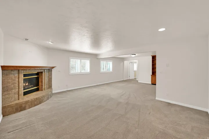 Spacious room featuring a gas fireplace with a stone surround, built-in shelving, recessed lighting, and multiple windows with plantation shutters
