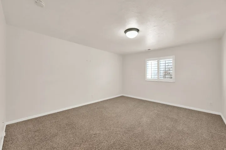 Carpeted room featuring a ceiling-mounted light fixture, a window with plantation shutters, and a white trim