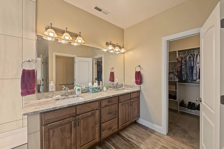 Dual vanity with wood-finish cabinetry, stone countertop, and integrated sinks