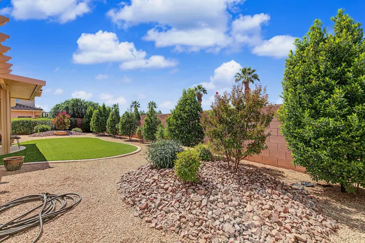 Manicured backyard with artificial turf, mature trees, and a rock-landscaped border