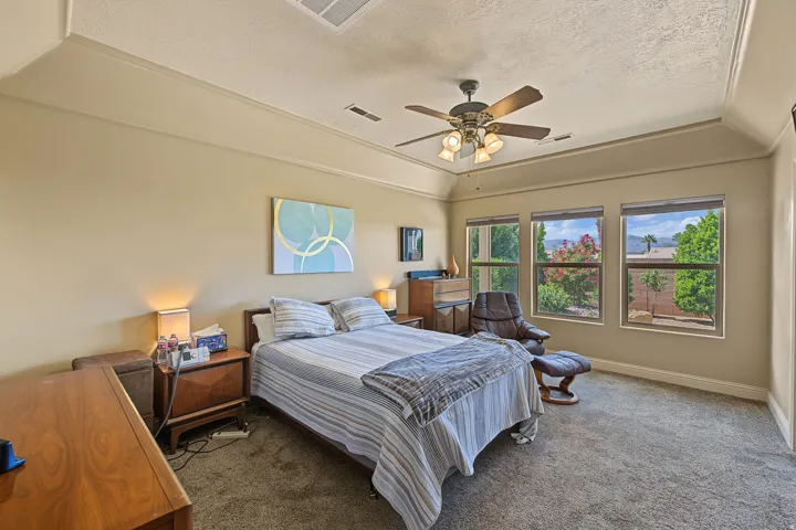Tray ceiling with crown molding, ceiling fan with light fixture, three large windows, and wall-to-wall carpeting