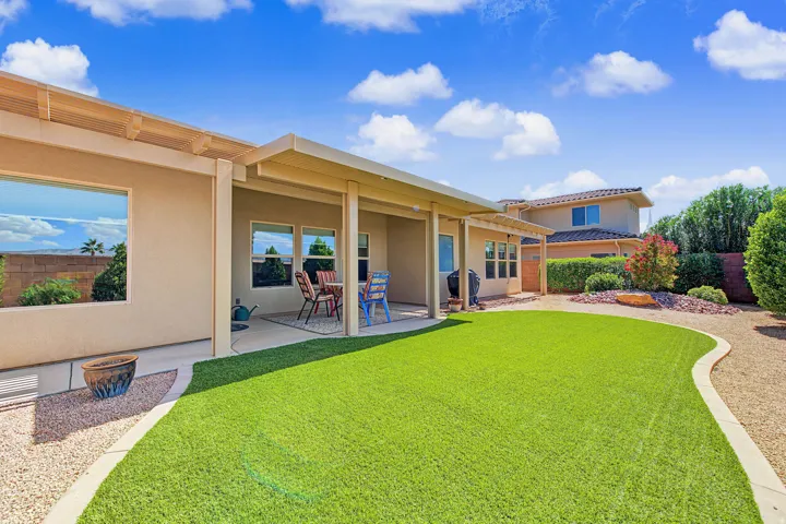 Expansive backyard featuring a covered patio, artificial turf lawn, xeriscape landscaping, and gravel pathways