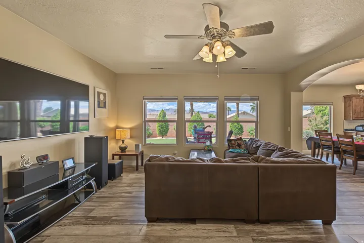 Open-concept living area featuring wood-finish flooring, a ceiling fan with integrated lighting, and multiple windows