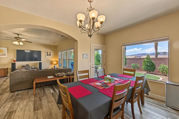 Dining area with wood-finish flooring, a decorative chandelier, and a large window overlooking a landscaped backyard with mountain scenery