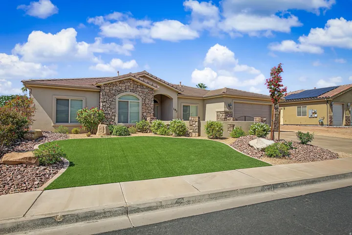 Stucco exterior with stone accents, arched entry, well-maintained artificial turf, xeriscape landscaping, and attached garage