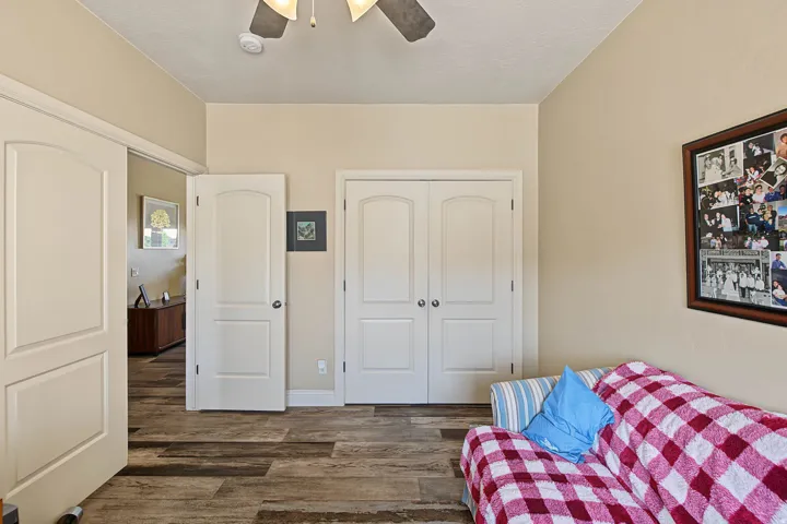 Wood-finish flooring, two-panel interior doors, and a ceiling fan with integrated lighting