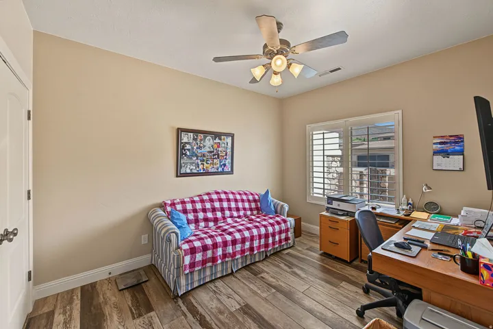 Wood-finish flooring, ceiling fan with integrated lighting, window with louvered shutters, and a paneled door