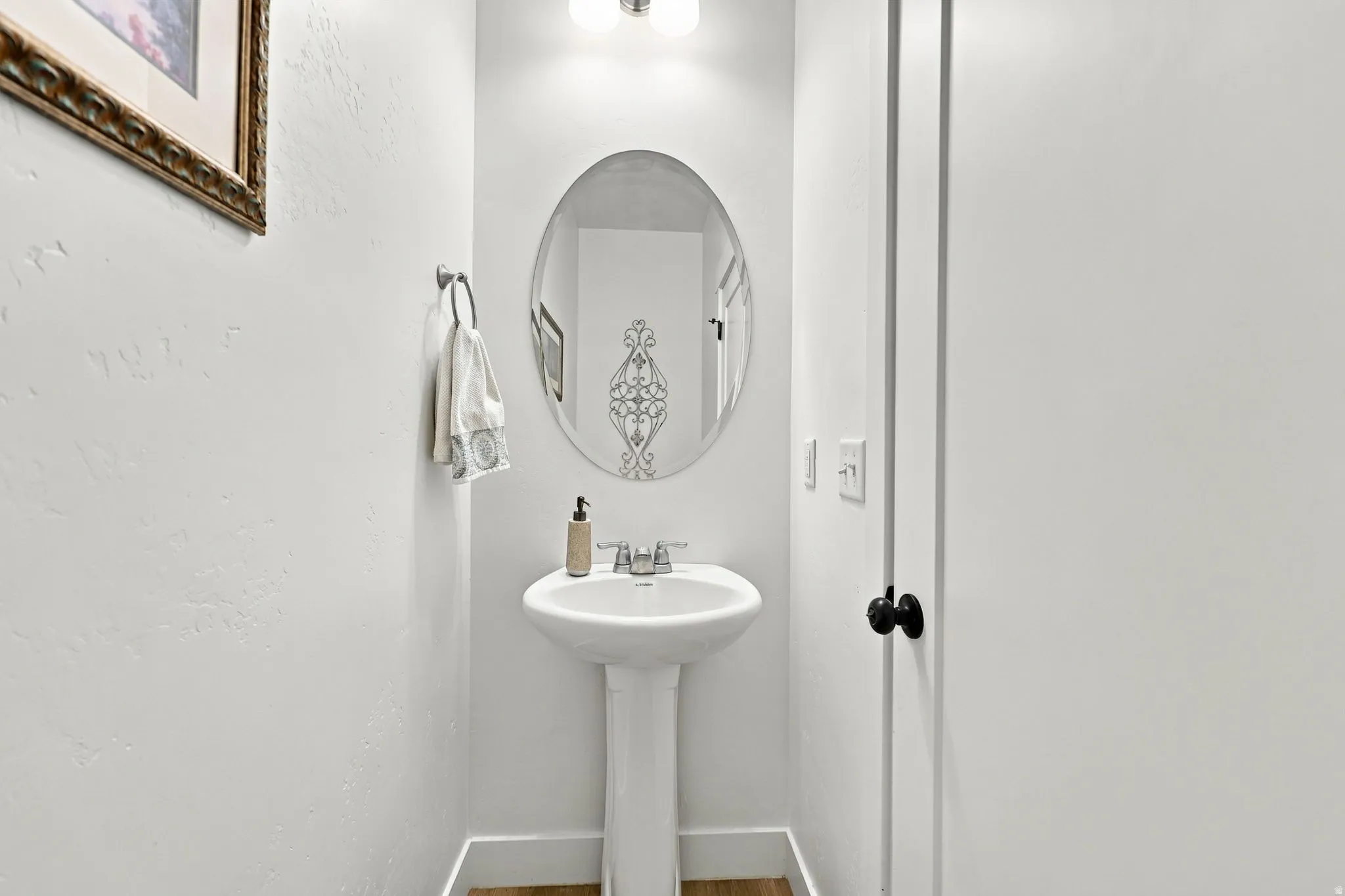 Pedestal sink with chrome faucet, oval mirror, and wall-mounted light fixture
