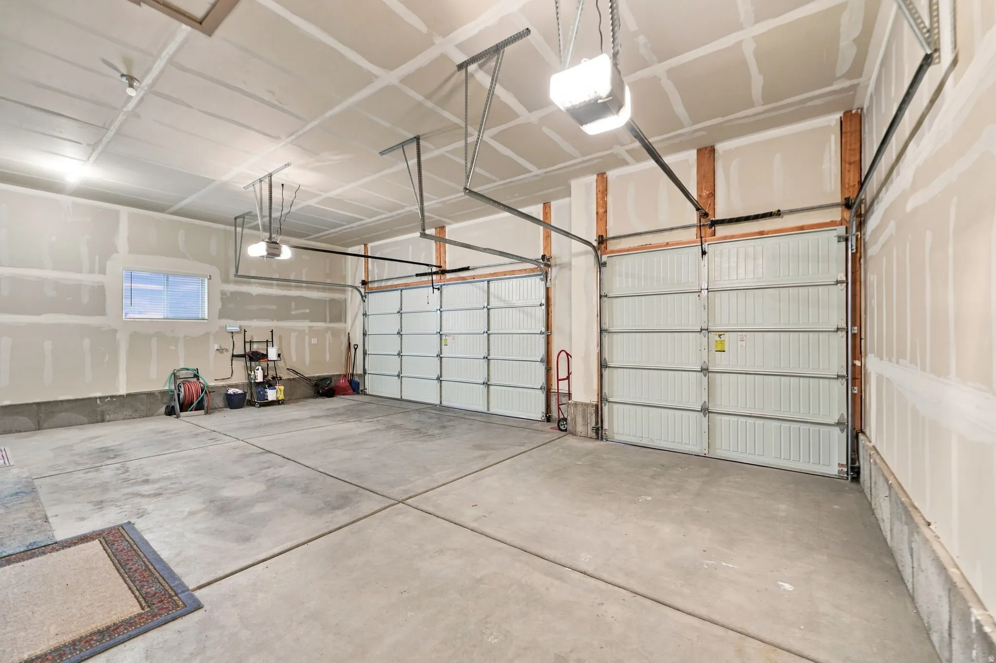 Two white garage doors with automatic openers, a concrete floor, and overhead lighting
