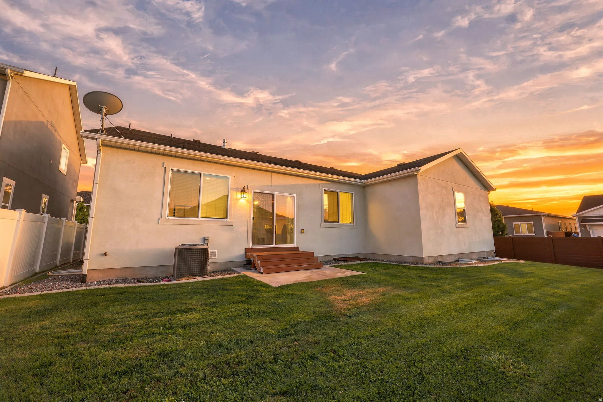 Stucco exterior with a pitched roof, featuring a sliding glass door, an exterior light fixture, and a white privacy fence