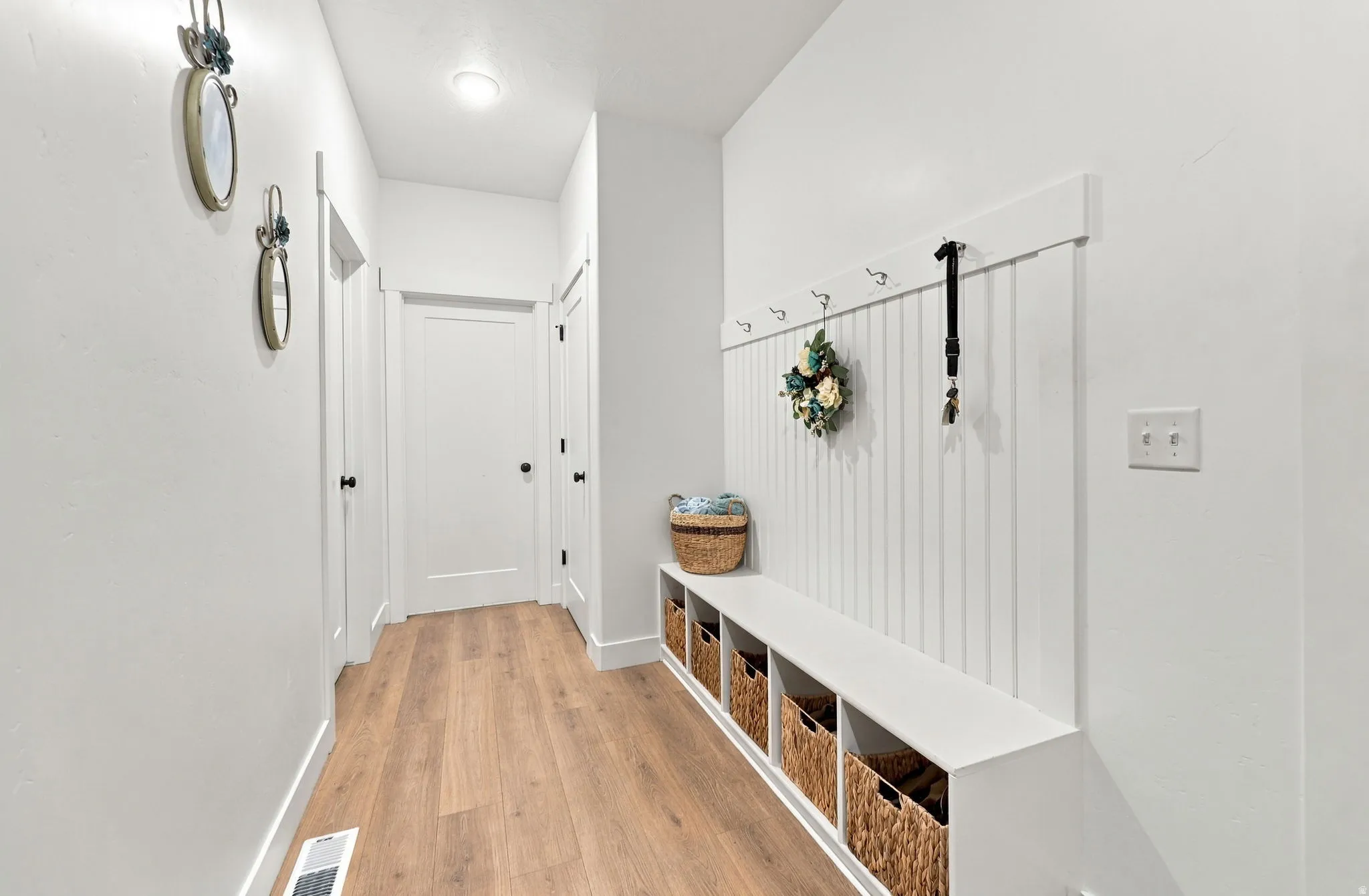 Wood-finish flooring, built-in storage bench, paneled wall with hooks, and recessed lighting