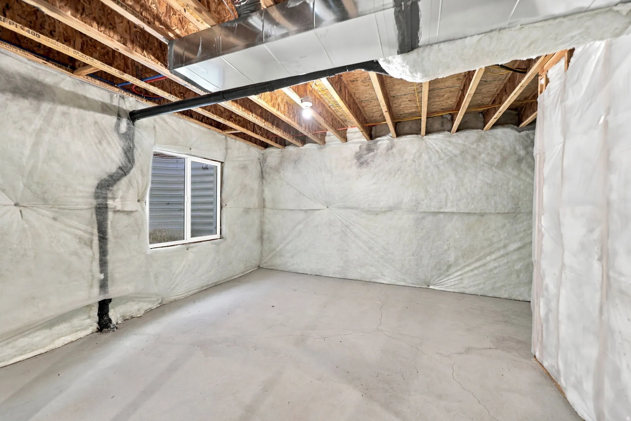 Unfinished lower level featuring exposed ceiling joists, concrete flooring, and a single egress window